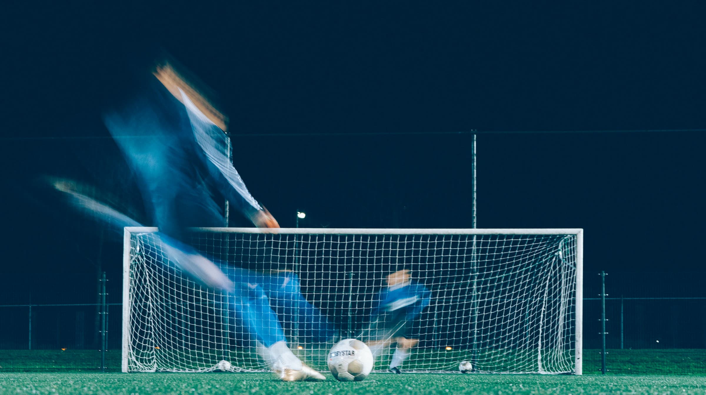 A goalkeeper diving to make a save under floodlights